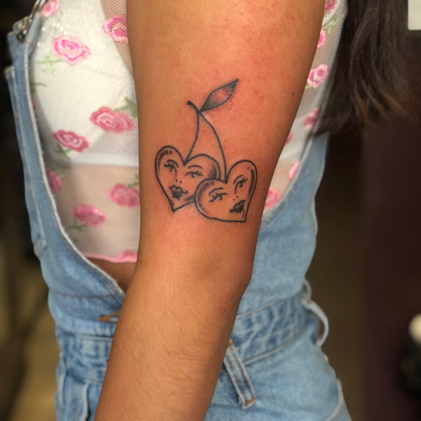 Tattoo of two hearts with faces and a single stem on an upper arm