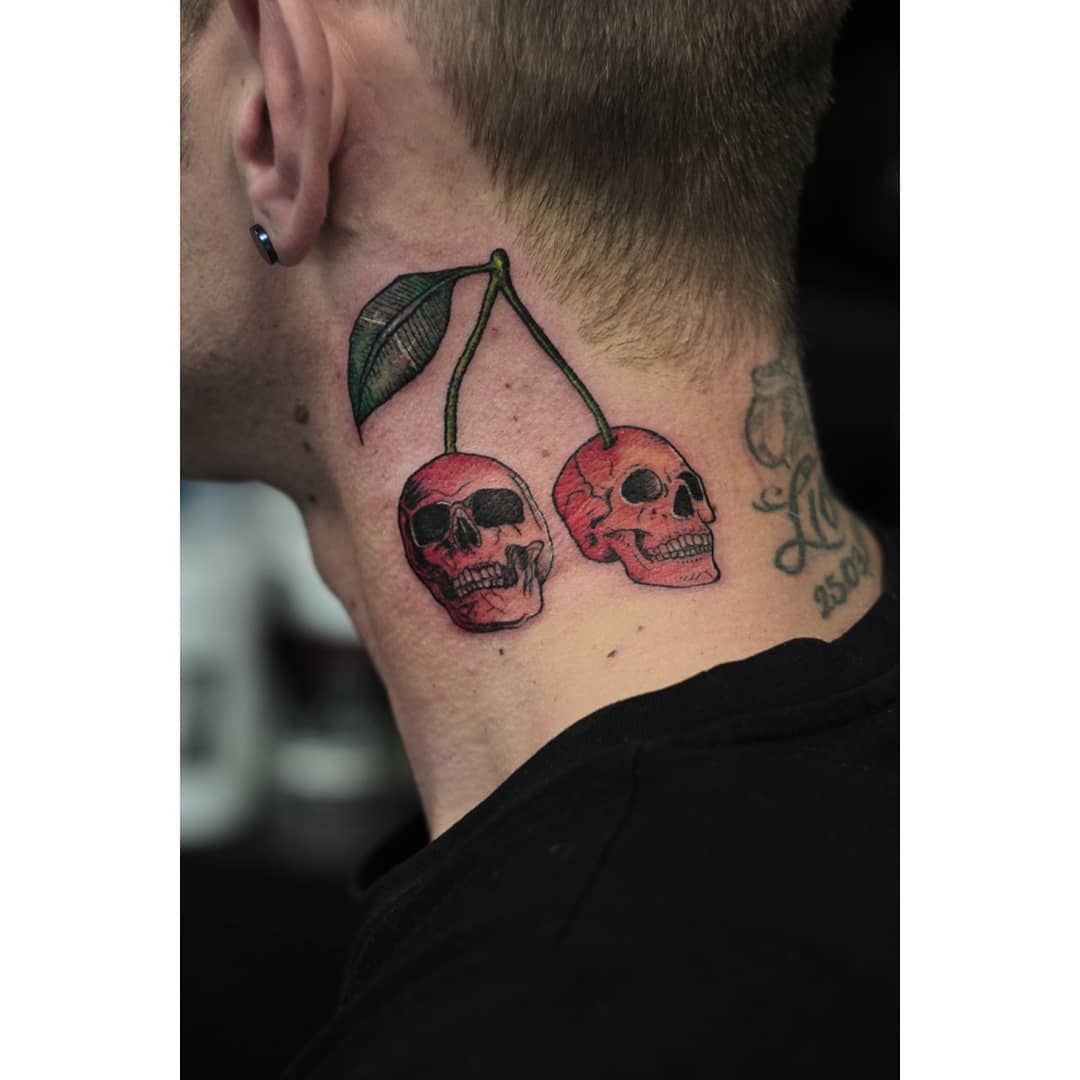 Neck tattoo of two cherries with skulls inside, connected by a green leaf stem