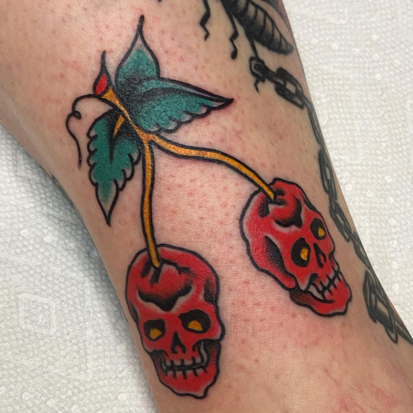 Tattoo of two red skulls connected by stems with green leaves on skin