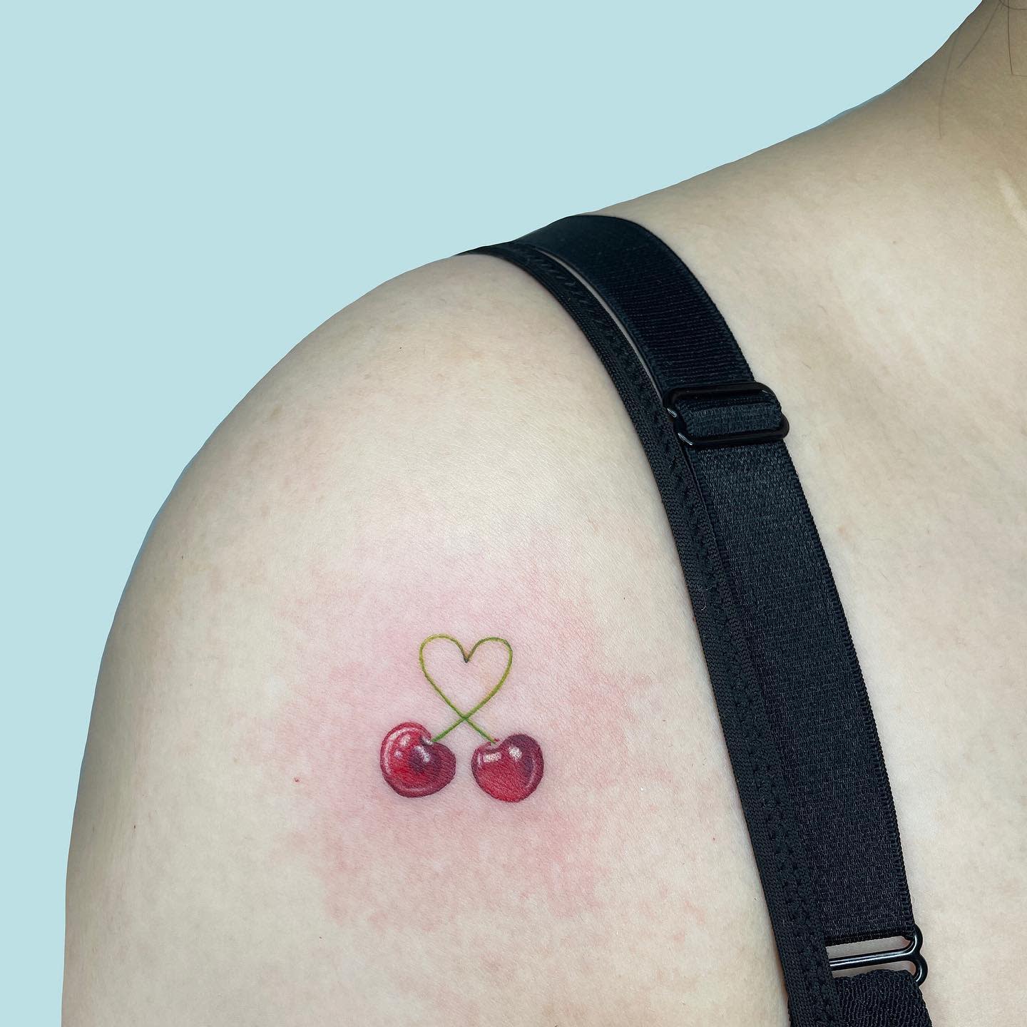 Tattoo of two cherries with stems forming a heart on a shoulder