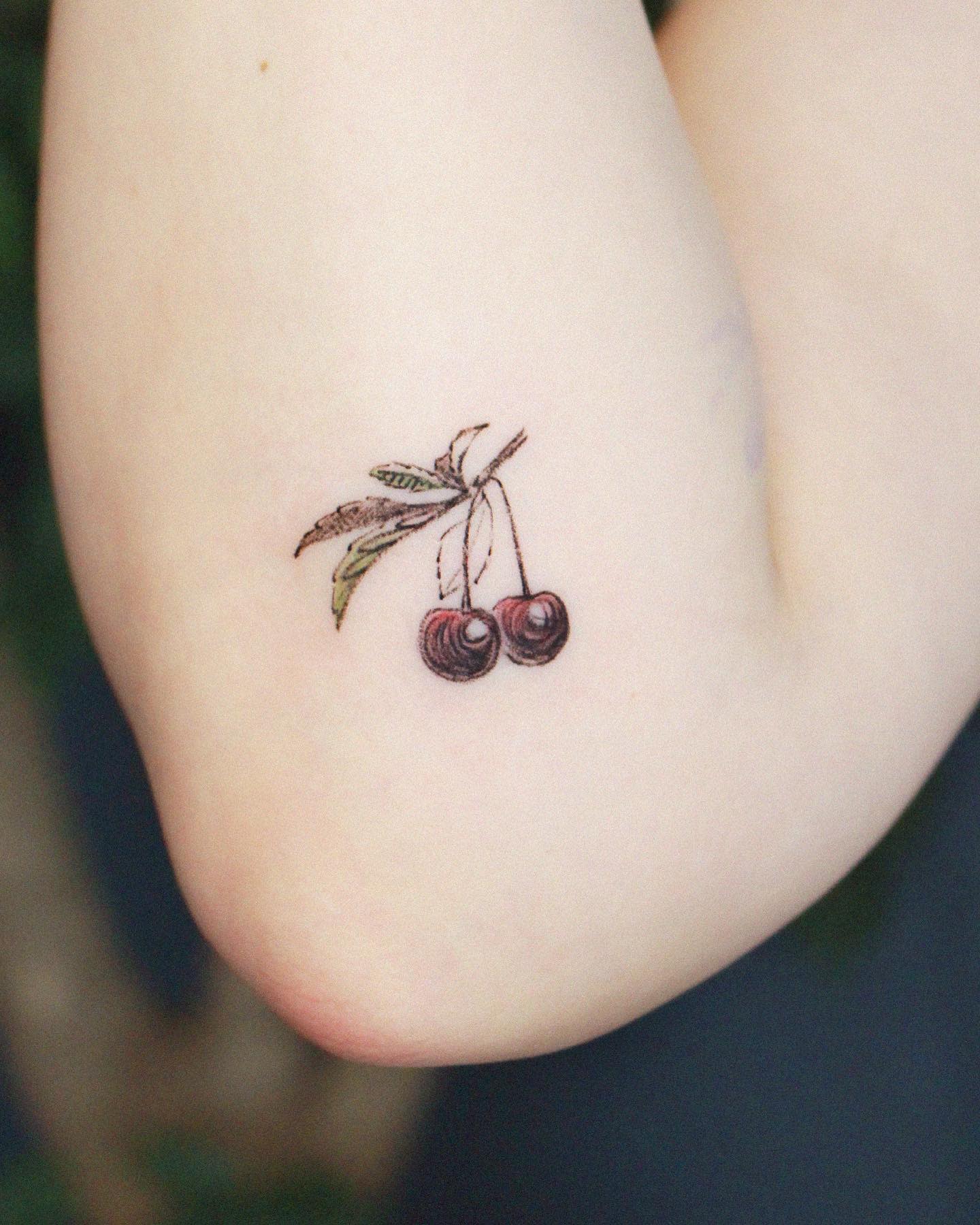 A tattoo of two cherries with leaves on an inner arm