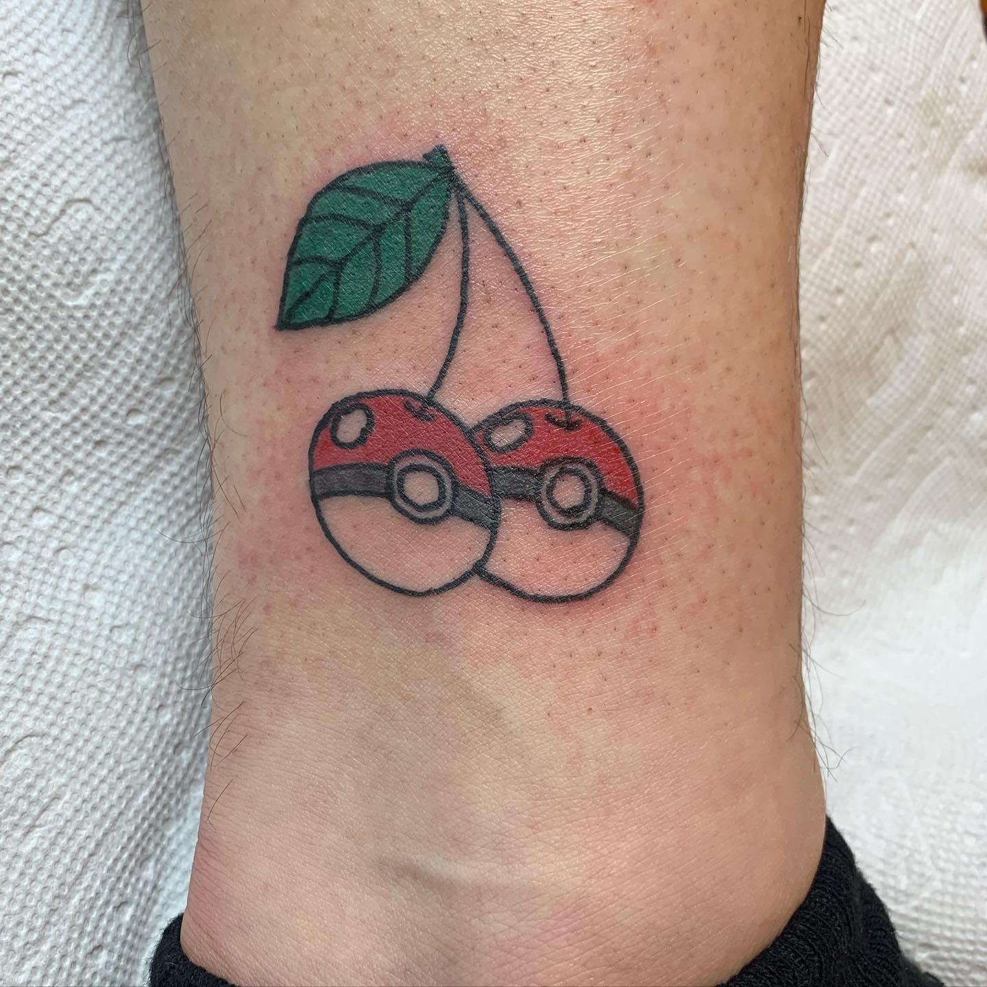Tattoo of two Poké Balls designed as cherries with a green leaf on an ankle