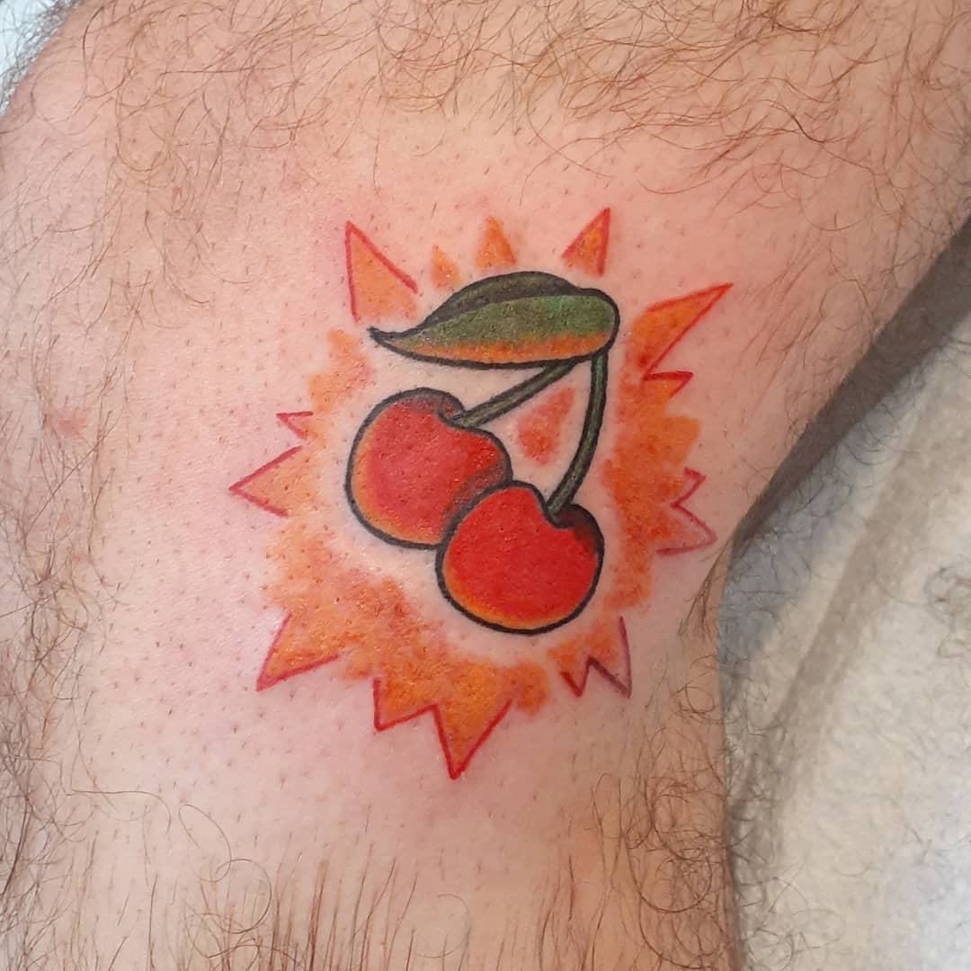 Bright red cherry tattoo with green leaves, set on a red burst background on skin