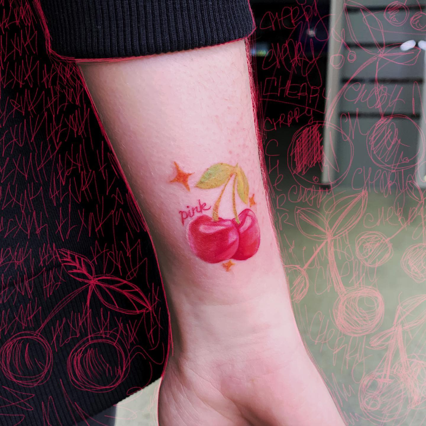 Arm tattoo of two cherries with green leaves and the word "pink"