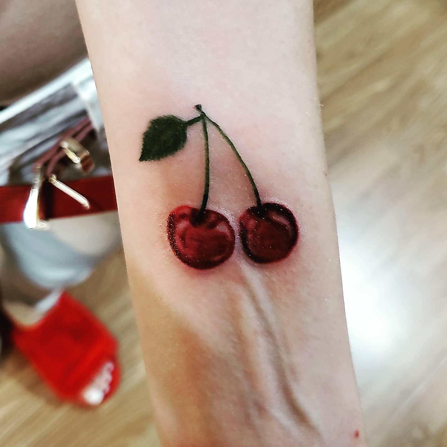 A tattoo of two cherries with a green leaf on a forearm