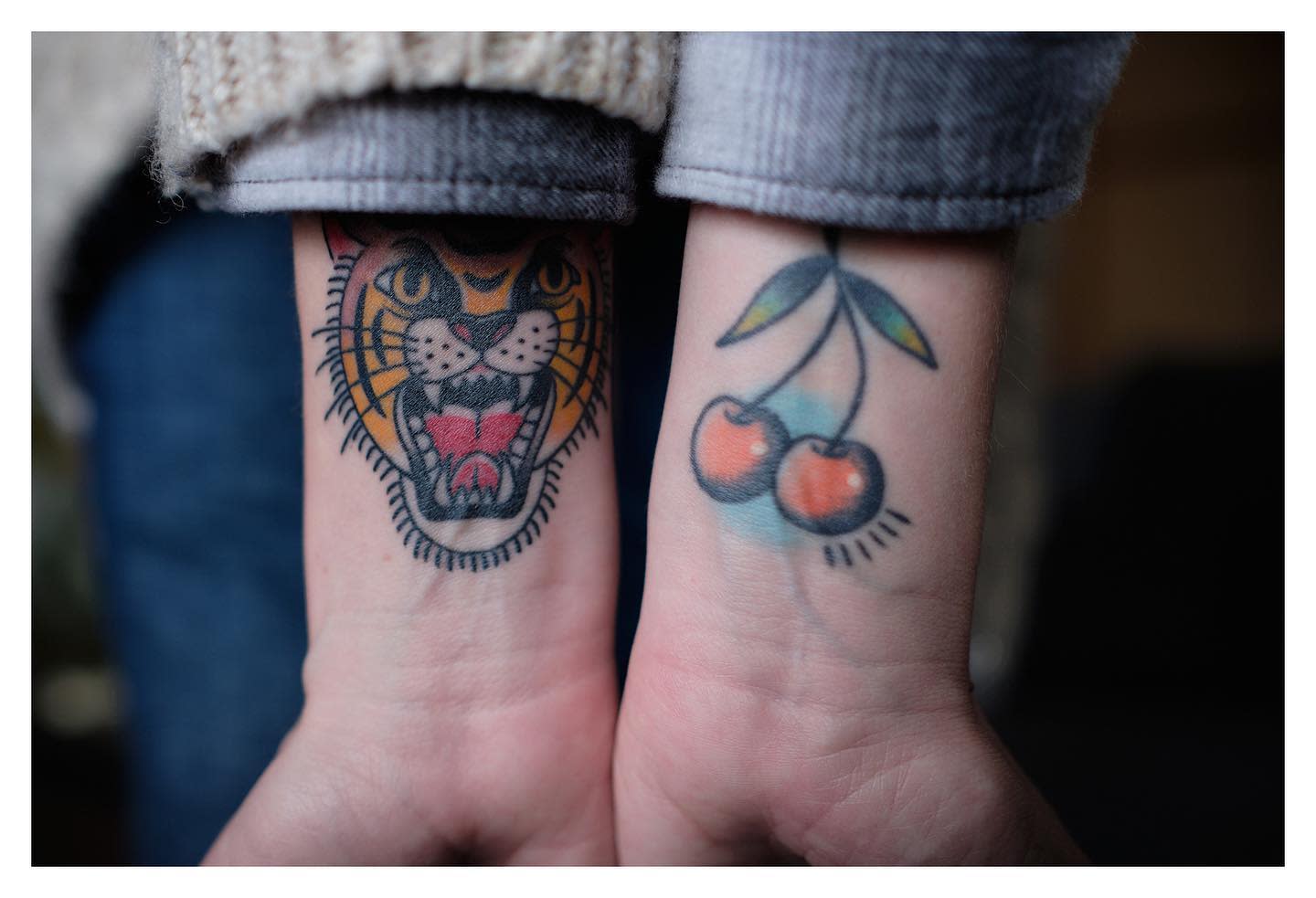 Close-up of arms with tiger head and cherries tattoos on the inner wrists