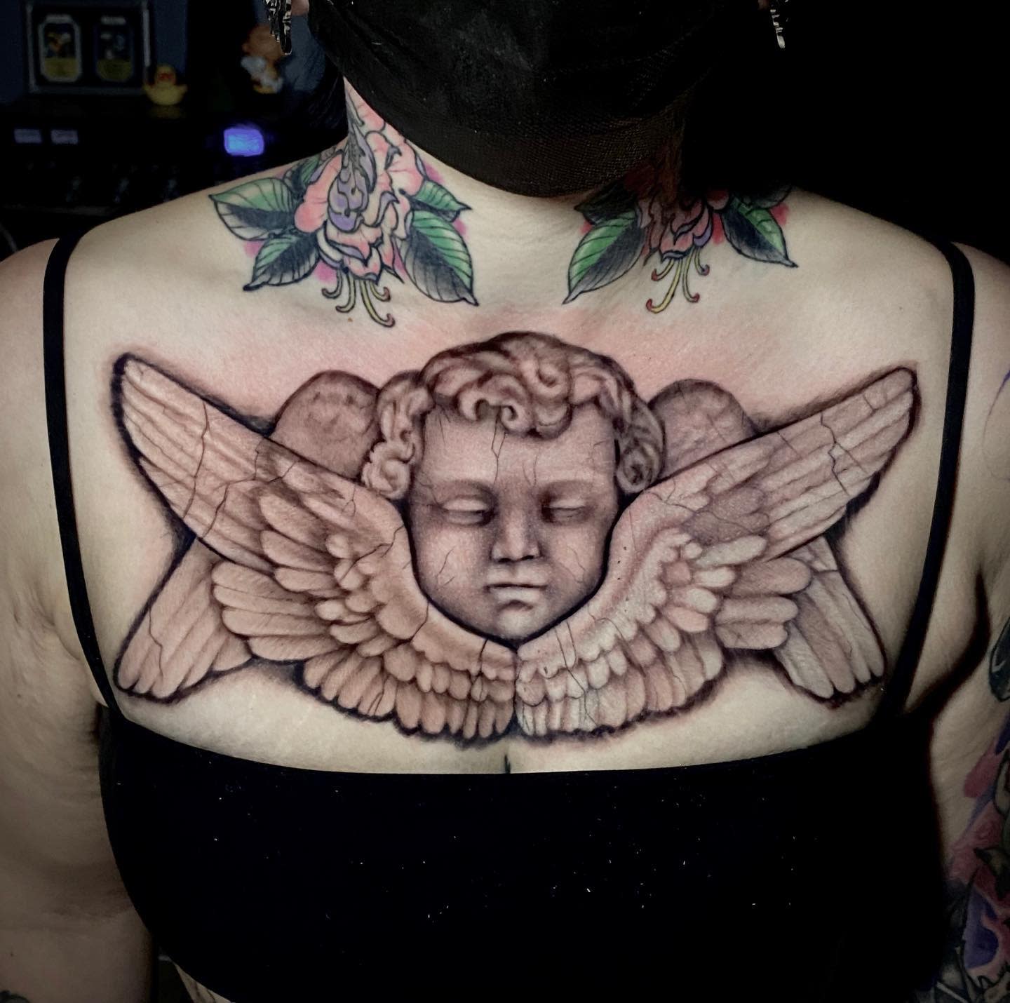 A large cherub face and wings tattoo across the chest, under collarbones
