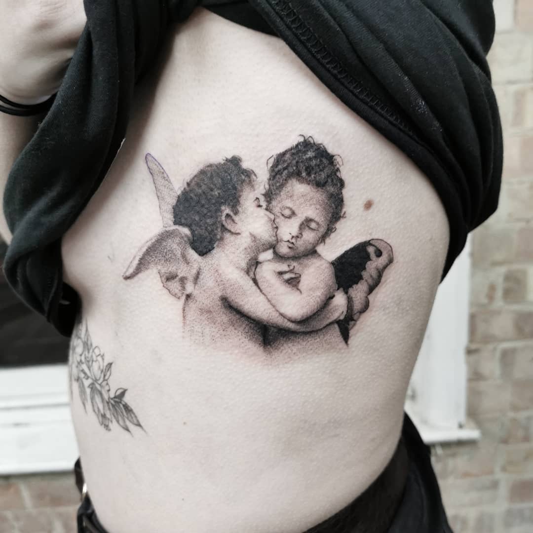 Tattoo of two cherubs; one kisses the other's cheek on side torso