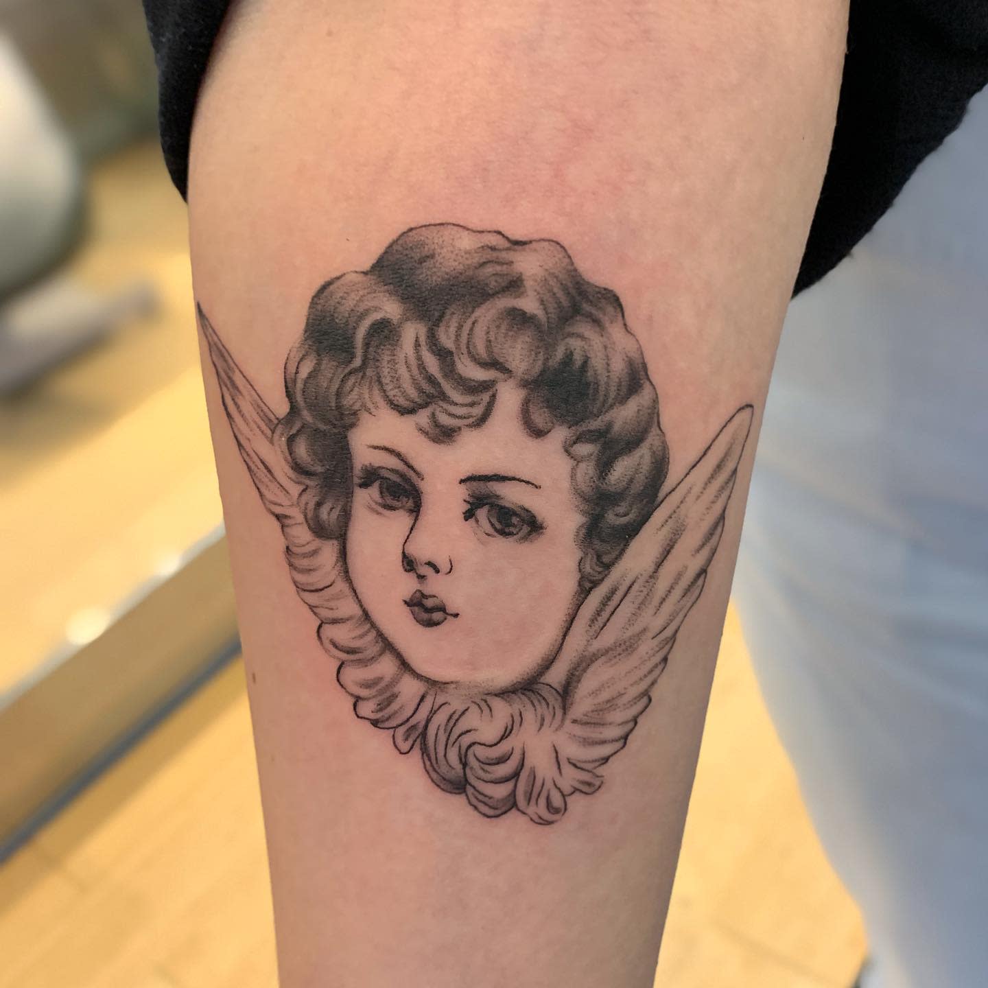 Tattoo of a cherubic child's face with wings on an upper arm
