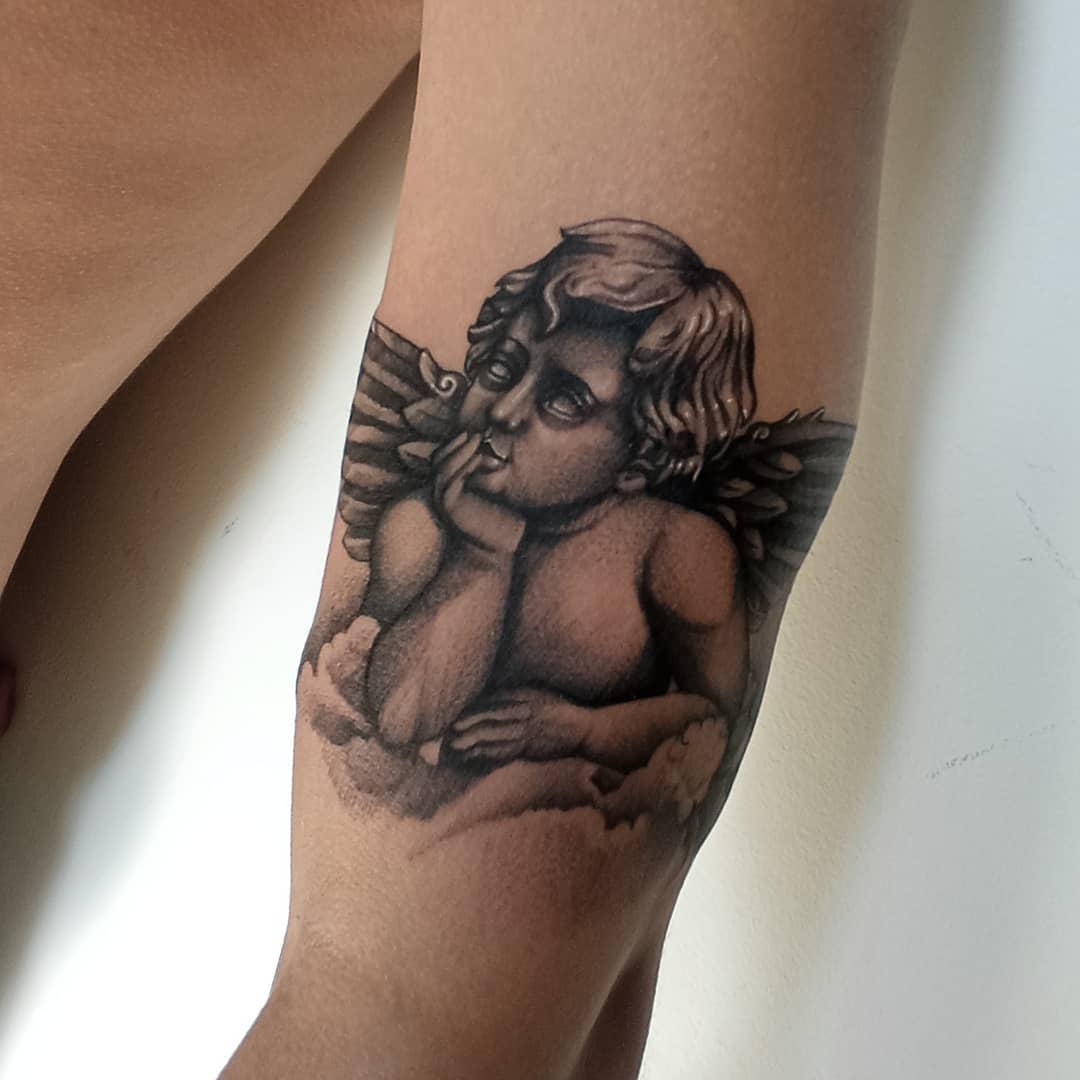 Tattoo of a cherub with wings resting on a cloud on the inner forearm
