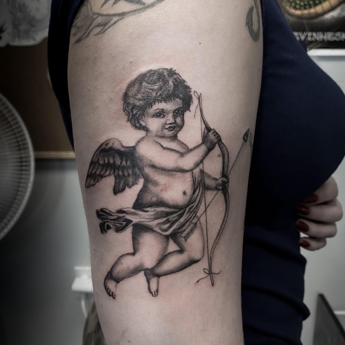A tattoo of a Cupid holding a bow and arrow on an upper arm