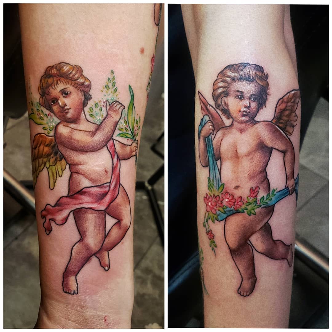 Two tattoos of cherubs on arms, adorned with ribbons and holding flowers and leaves
