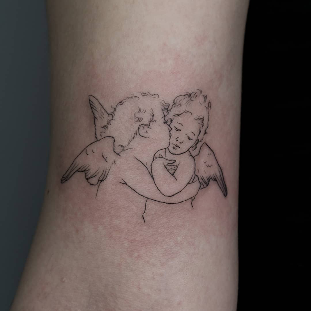Tattoo of two cherubs with wings, one kissing the other's cheek