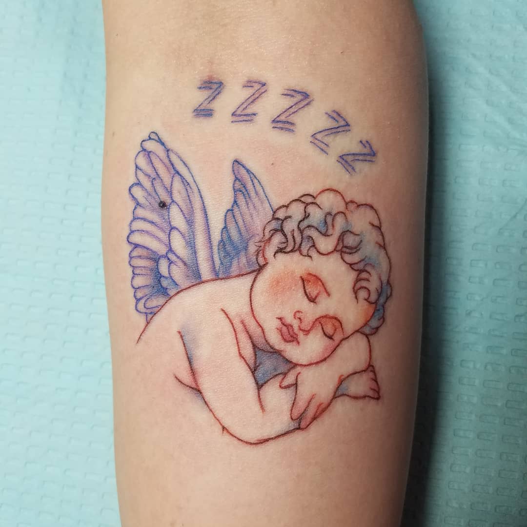 Tattoo of a sleeping cherub with wings and Z's above its head on light skin