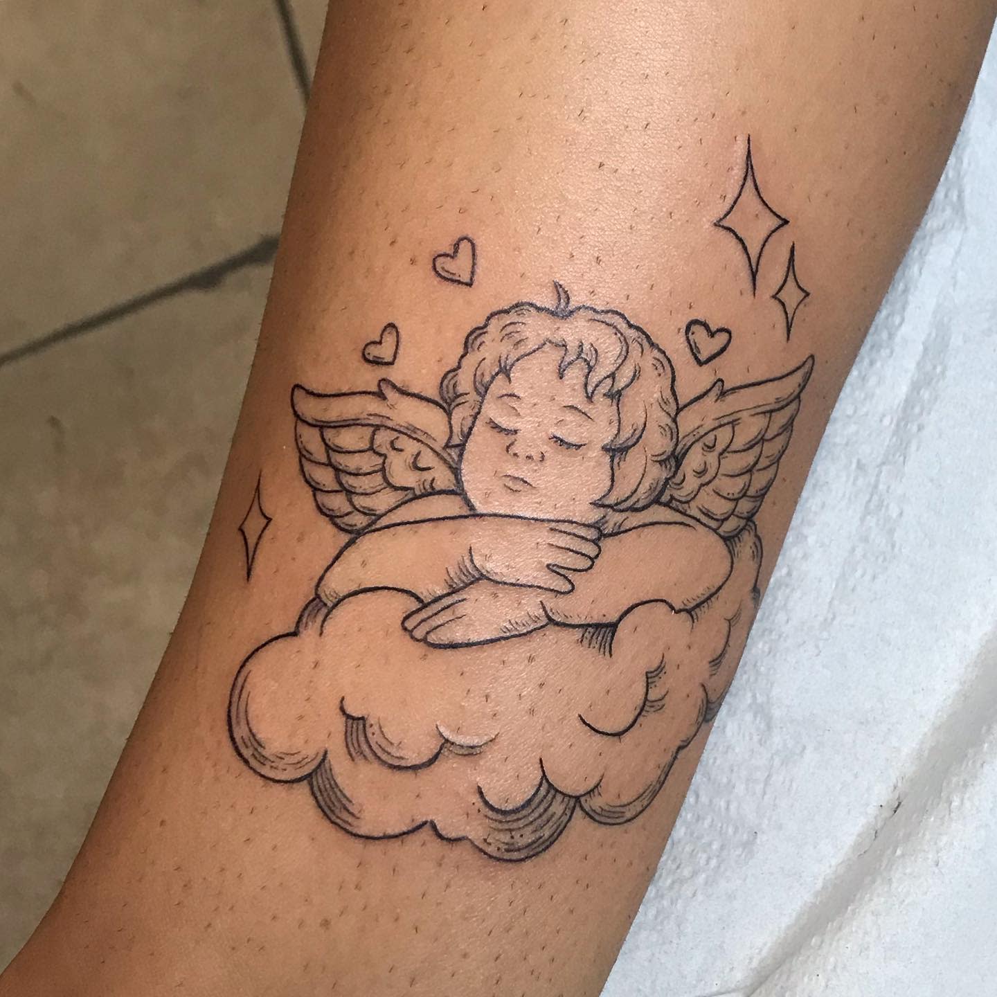 Tattoo of a sleeping cherub on a cloud with hearts and stars on an arm