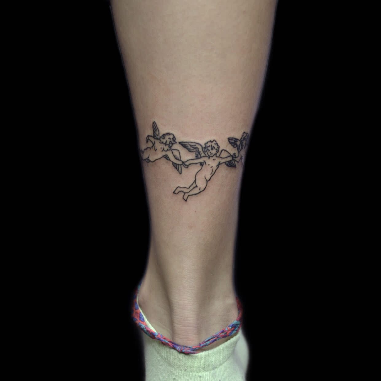 Tattoo of three small cherubs holding a ribbon on the back of a leg