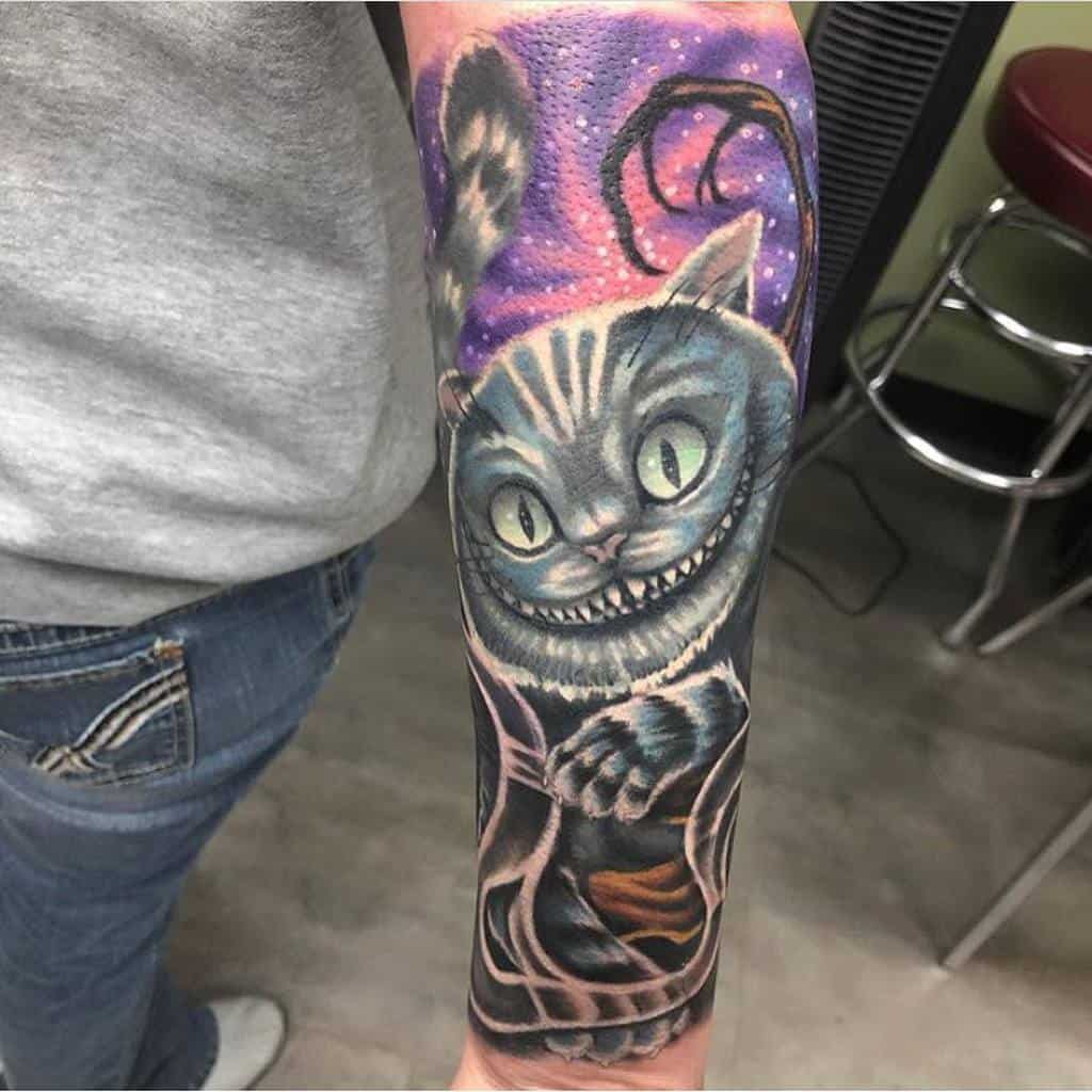A vibrant Cheshire Cat forearm tattoo with glowing eyes and a mischievous grin, set against a colorful sky