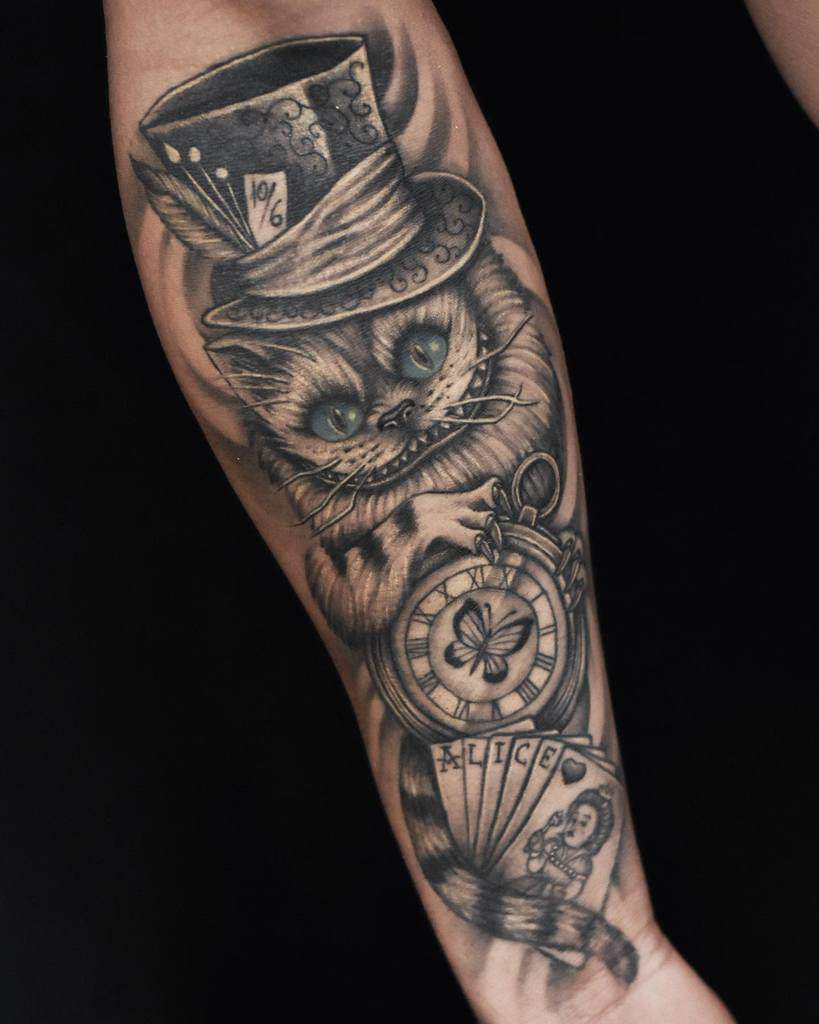 Black and grey Alice in Wonderland tattoo featuring the Cheshire Cat wearing a Mad Hatter hat, holding a pocket watch and Alice-themed cards