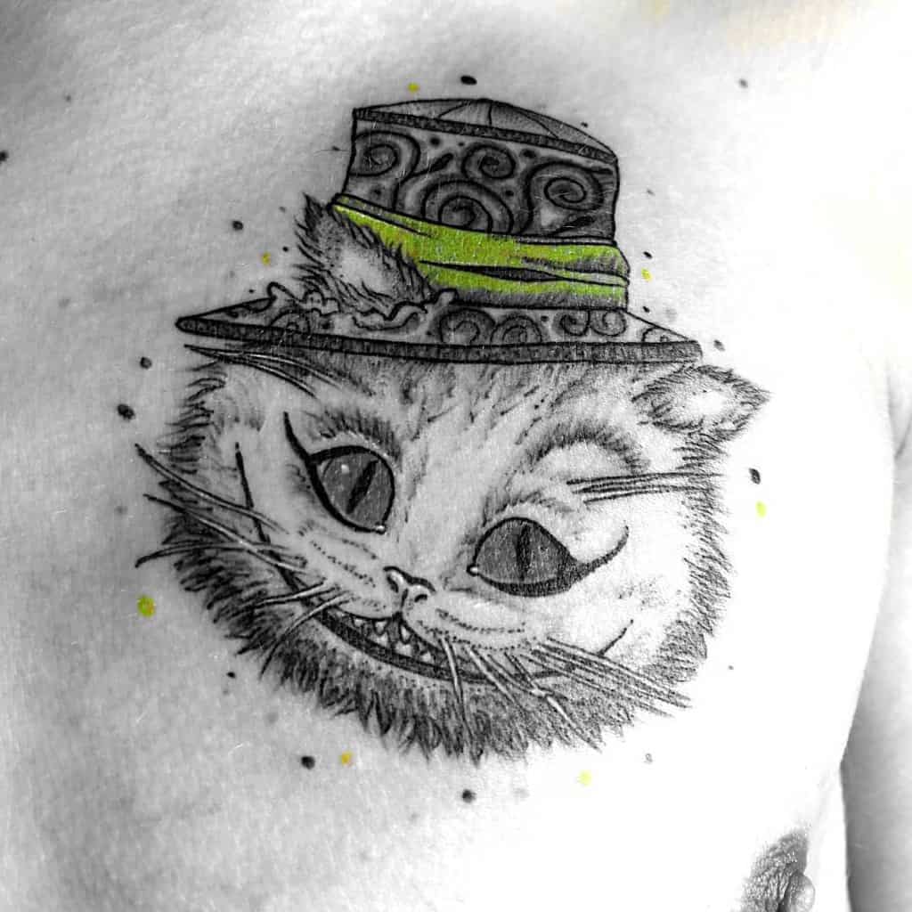 Black and white tattoo of the Cheshire Cat from Alice in Wonderland, with a brightly colored green hat and a playful grin