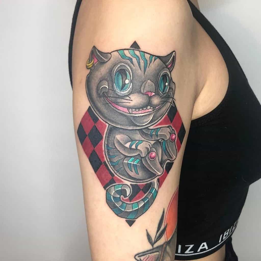 Vibrant tattoo of the Cheshire Cat from Alice in Wonderland, depicted in a playful, cartoonish style with bright teal stripes, a diamond-shaped background, and a wide grin