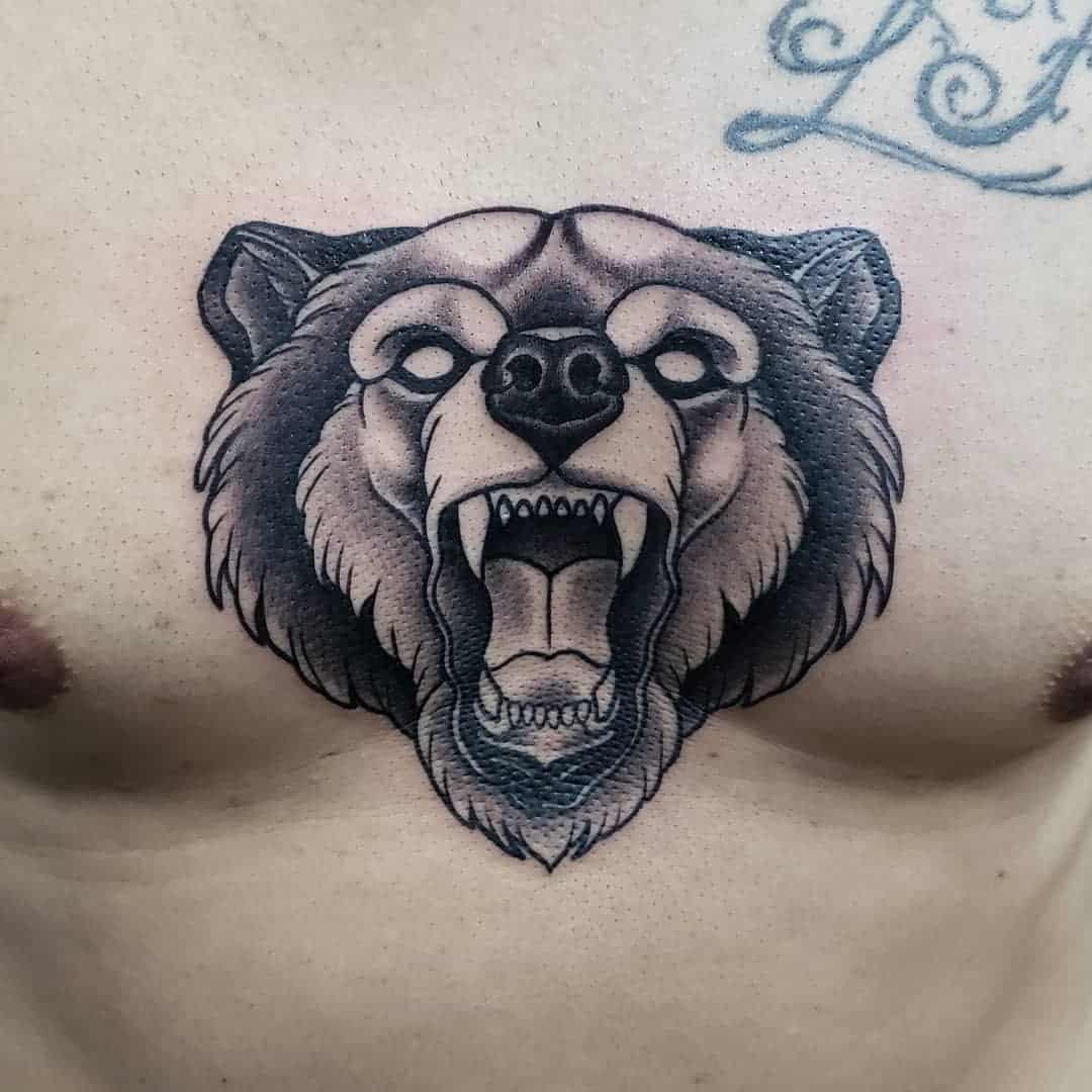 Tattoo of a fierce bear head with an open mouth on a person's chest