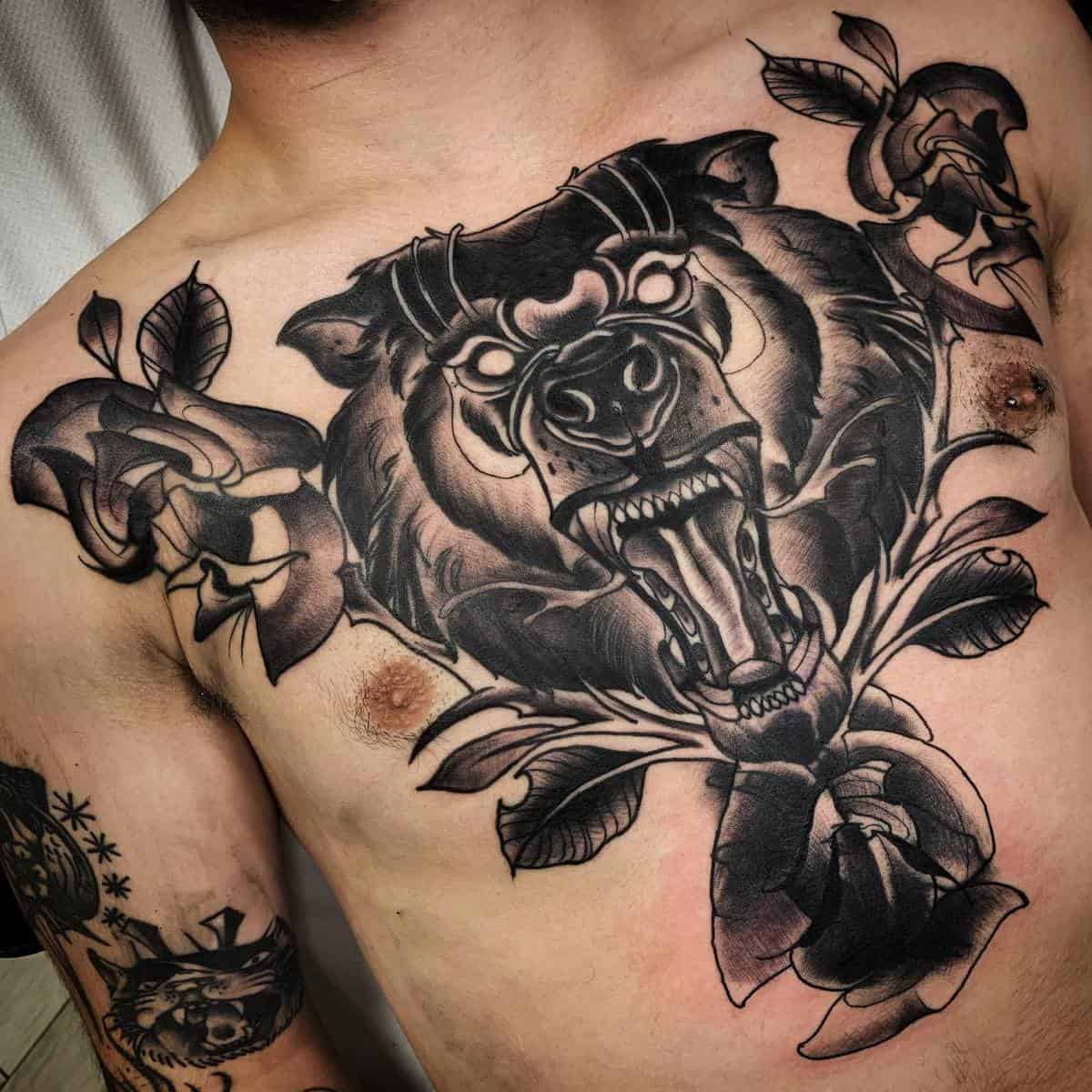 A detailed chest tattoo of a roaring bear surrounded by intricate flowers and leaves