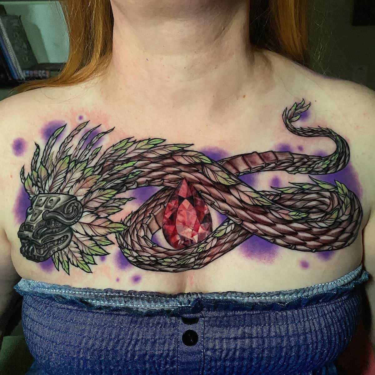 Colorful Quetzalcoatl chest tattoo with vibrant feathers and a large red gemstone at the center