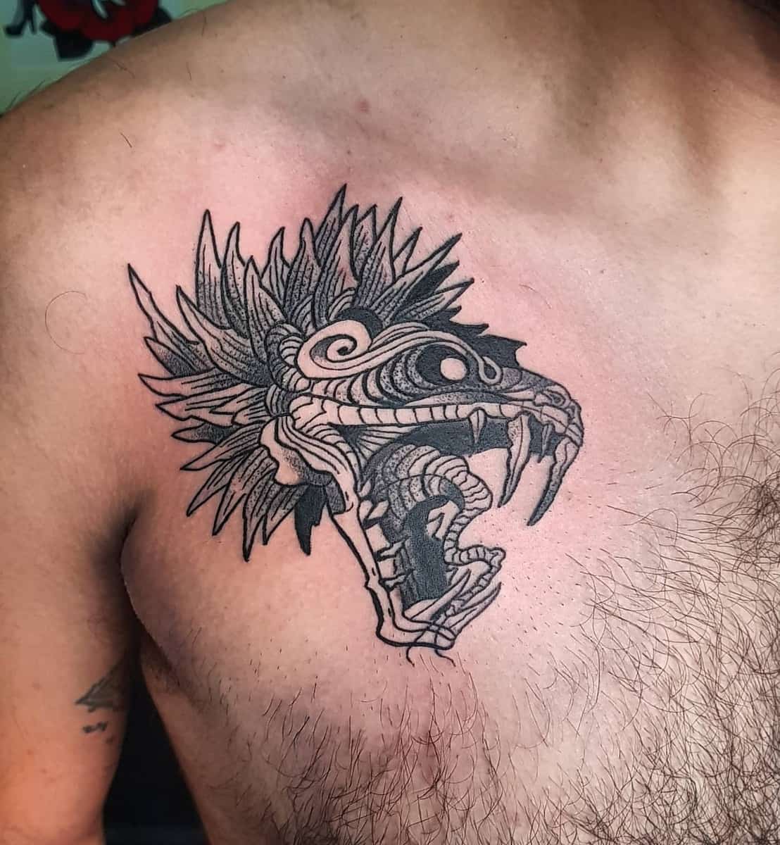 Bold Quetzalcoatl chest tattoo featuring a detailed feathered serpent head with fangs