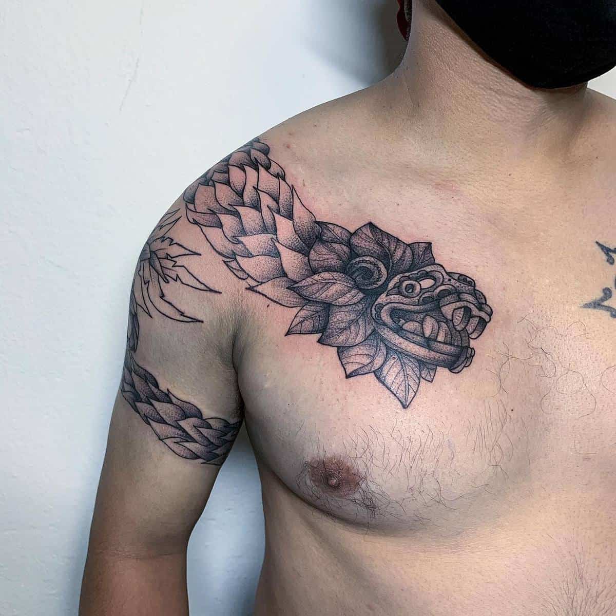 Black ink Quetzalcoatl tattoo with a detailed feathered serpent head and body wrapping across the shoulder