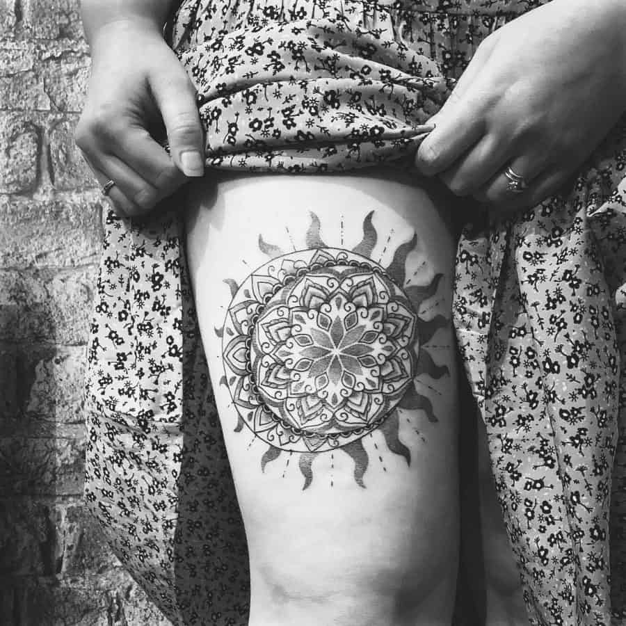 Intricate black ink mandala sun tattoo on the thigh, featuring detailed geometric patterns and symmetrical shading for a bold, artistic look.