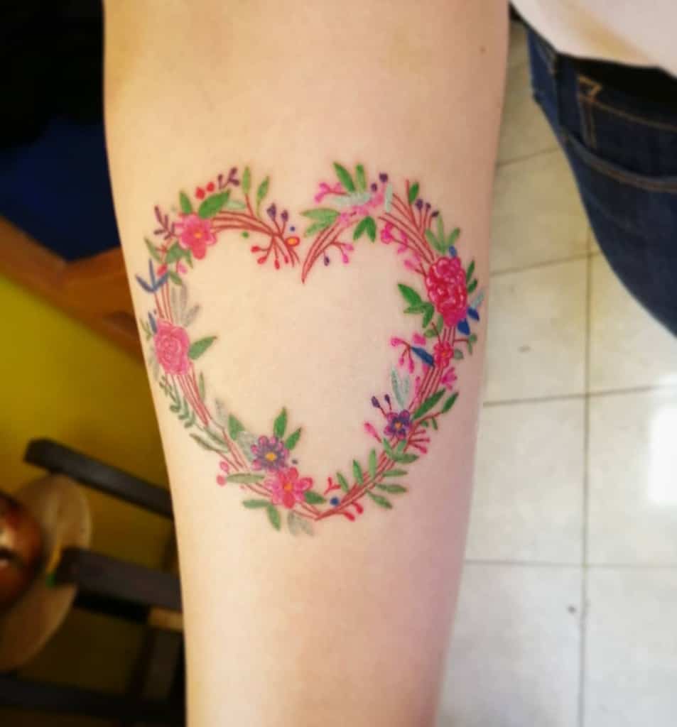 Tattoo of a heart-shaped wreath with colorful flowers and leaves