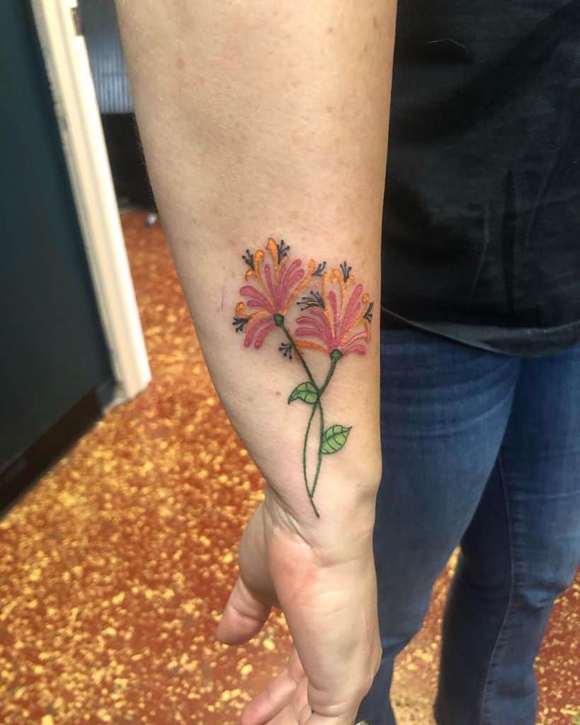 Small and colorful honeysuckle tattoo on the forearm, featuring bright orange and pink flowers
