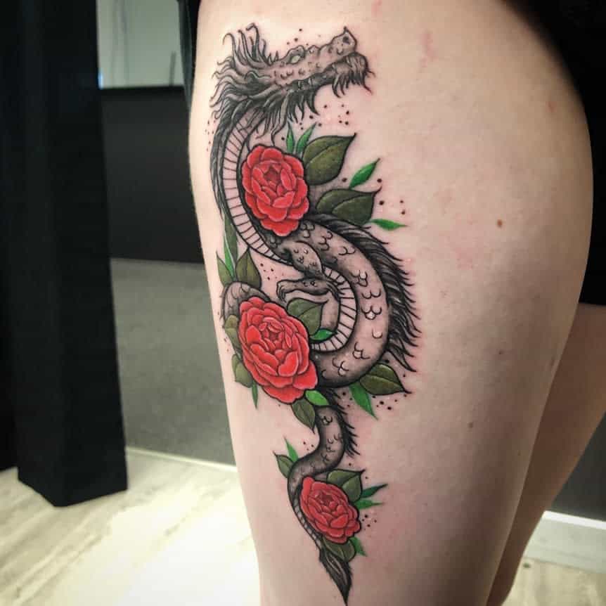 Tattoo of a dragon entwined with red roses and green leaves on a woman's thigh