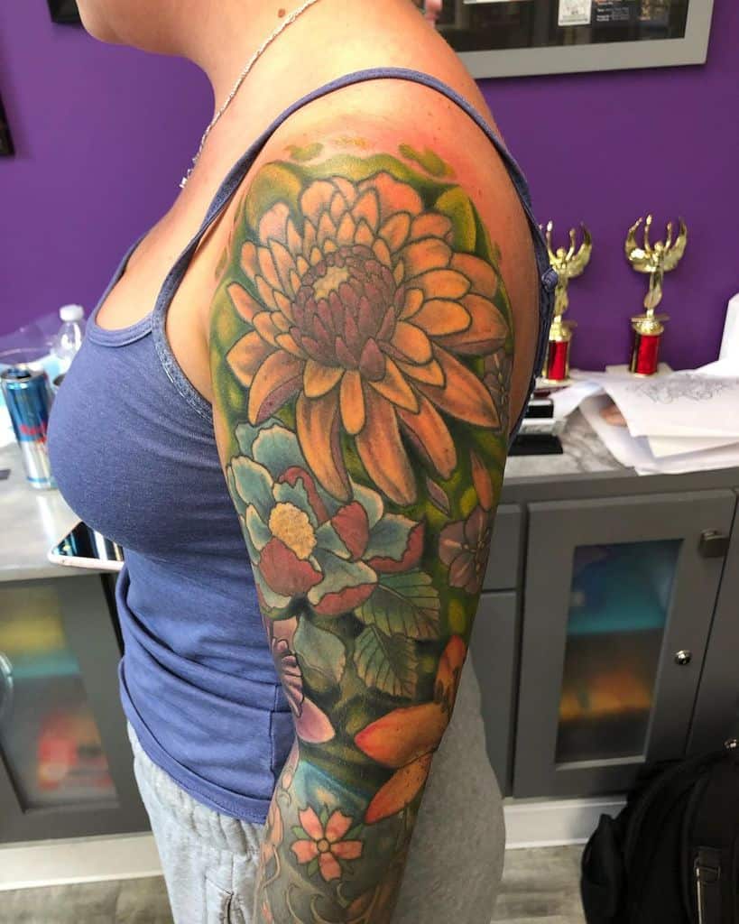 Vibrant full-sleeve tattoo featuring colorful flowers, including a large orange chrysanthemum, surrounded by lush green leaves