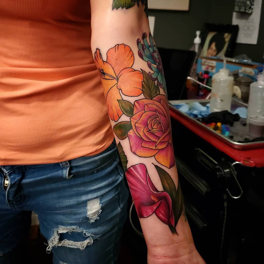 A vibrant floral tattoo sleeve graces the person's left forearm, showcasing an array of colorful blooms