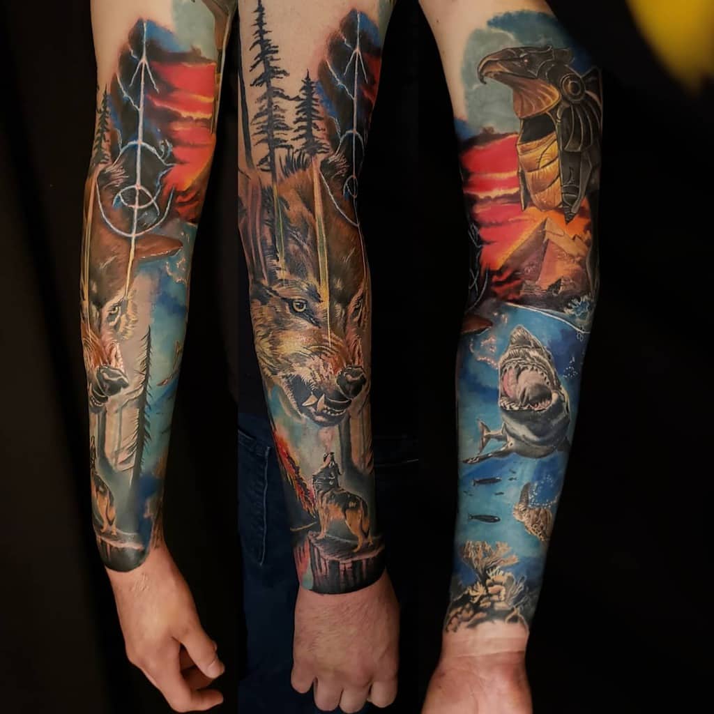 Vivid full-sleeve tattoo showcasing a dynamic forest theme with a wolf, eagle, shark, and captivating sunset