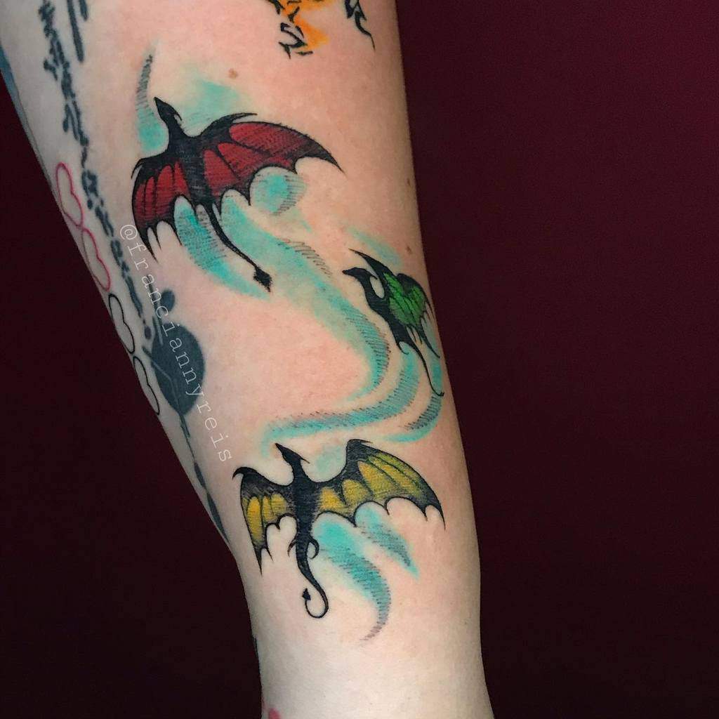 Tattoos of colored dragon-style creatures flying on an arm