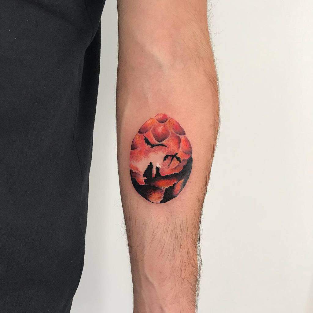 Forearm tattoo of a fantasy scene with a dragon in a red-orange egg shape