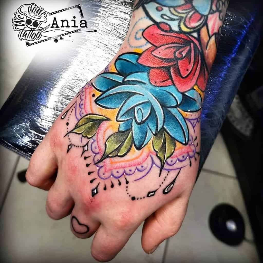 A bold tattoo featuring vibrant blue and red flowers, green leaves, intricate lace-like patterns