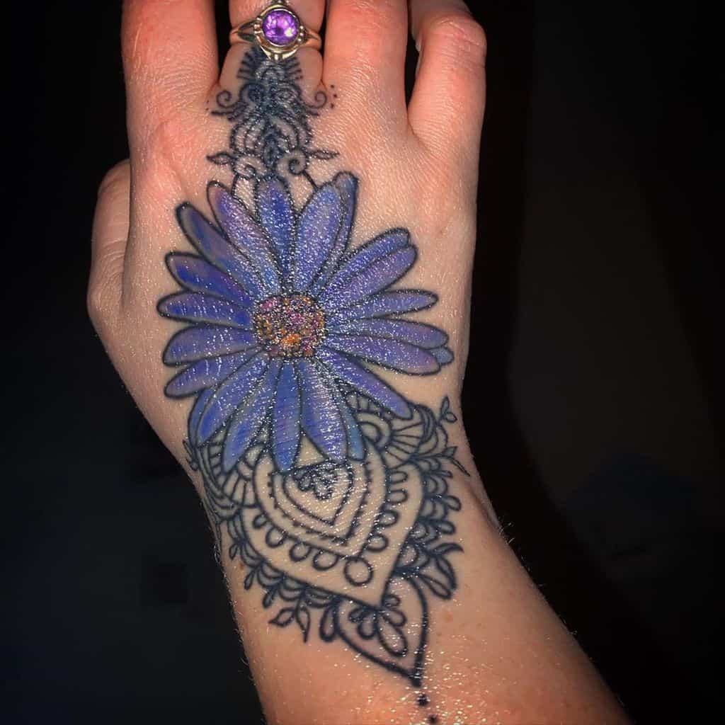 A stunning tattoo featuring a vibrant purple daisy with glittering details, intricate black lace patterns, and ornamental accents