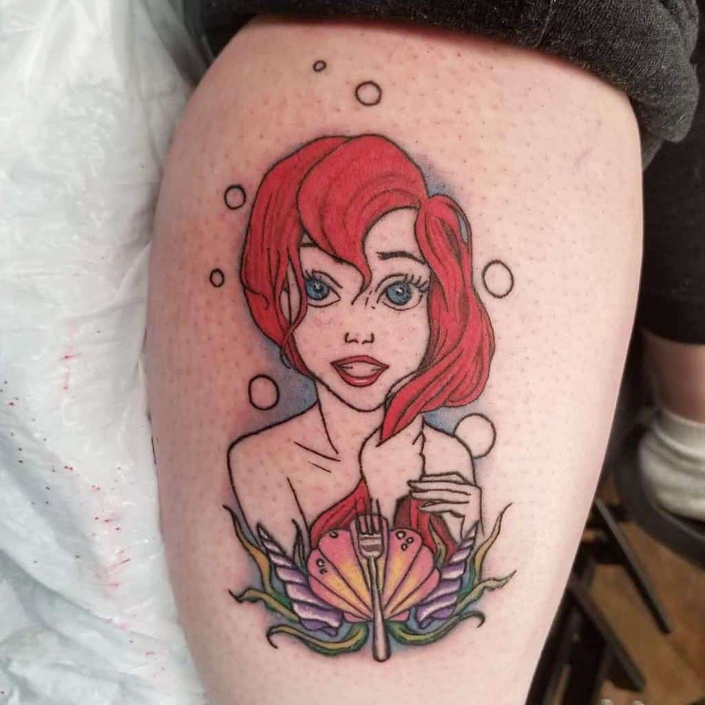A delicate tattoo of Ariel with her red hair, holding a fork, surrounded by bubbles and a colorful shell and seaweed design