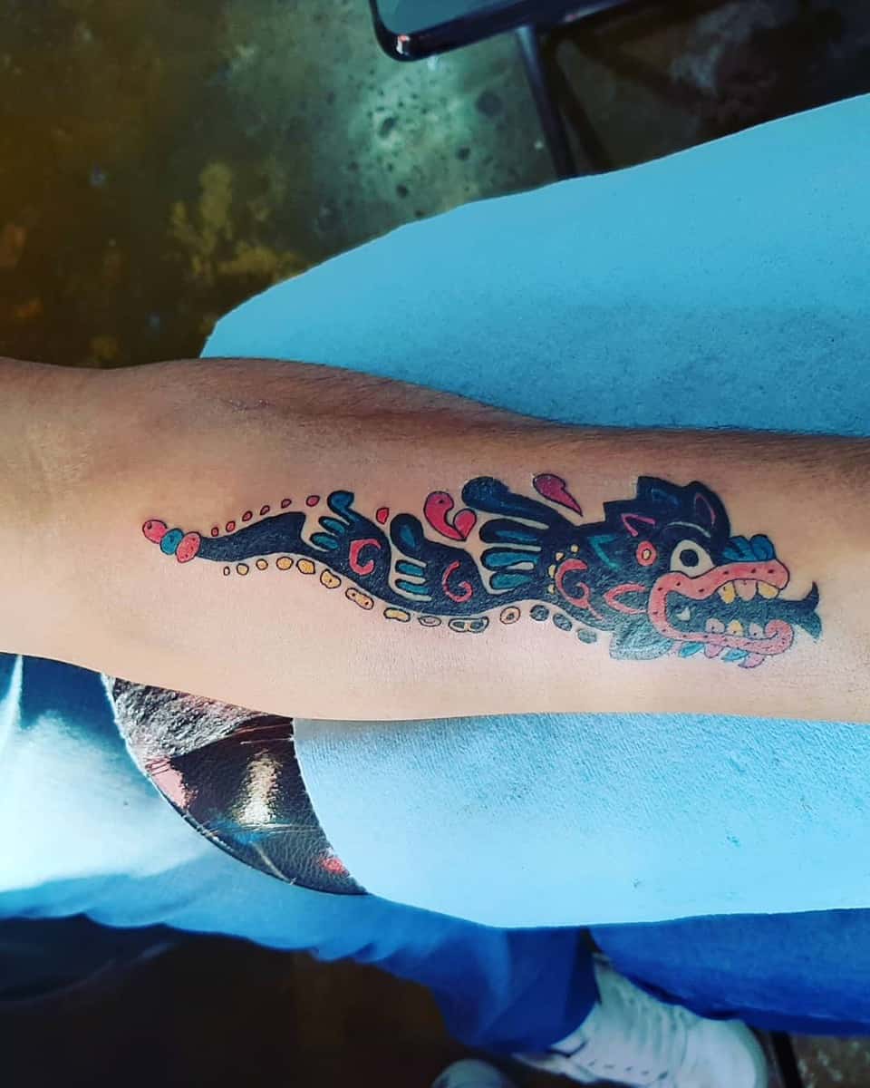 Colorful Quetzalcoatl tattoo with bold blue and red designs, featuring the feathered serpent