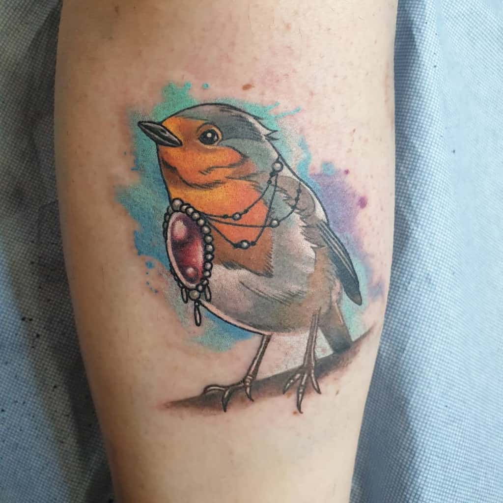 Colorful tattoo of a sparrow holding a jeweled pendant on an arm