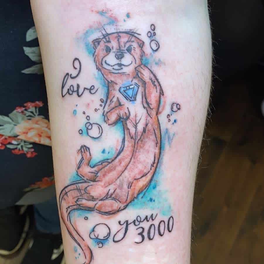 A tattoo of an adorable otter clutching a blue gem with bubbles floating around, featuring the text "I love you 3000" on someone’s arm