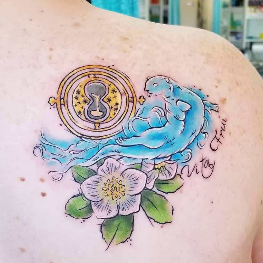 Elegant otter tattoo with vibrant blue hues, a golden compass, white flower, and Latin script, blending nature and symbolic elements