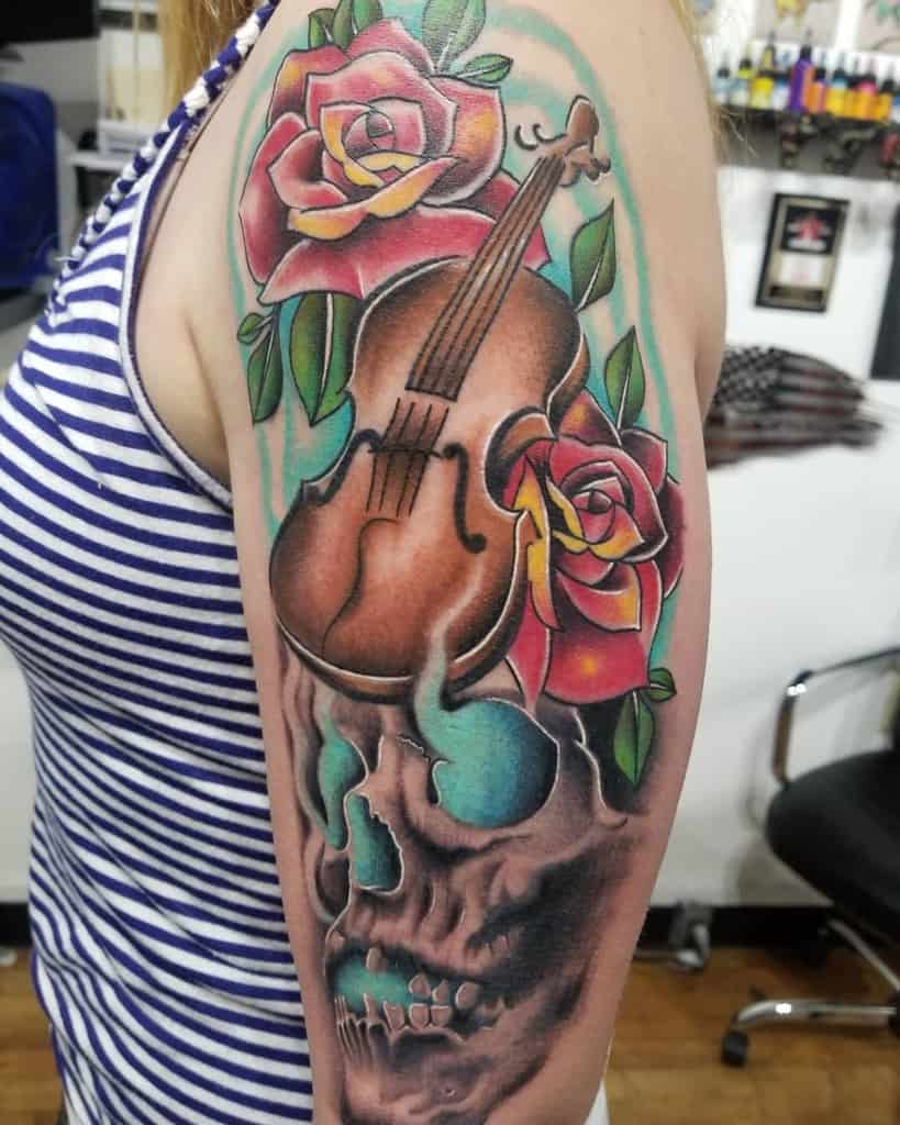Half sleeve tattoo of a violin, roses, and a skull on an upper arm