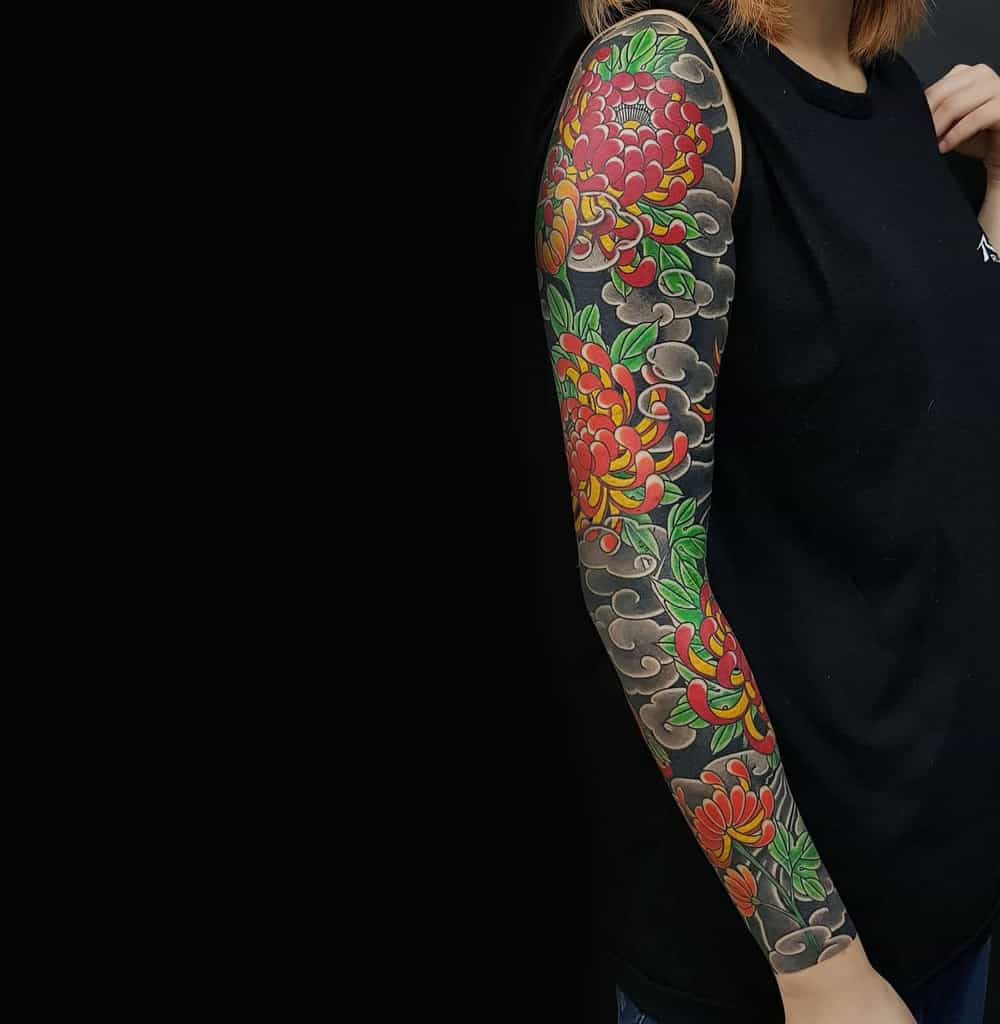 This vibrant Japanese sleeve tattoo showcases intricate chrysanthemum flowers in bold red and yellow hues, set against a smoky black background for a dynamic and captivating design