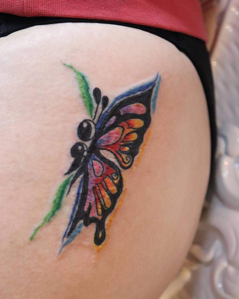 A colorful semicolon butterfly tattoo with vibrant shades of orange, pink, and blue, symbolizing transformation, mental health awareness, and personal strength