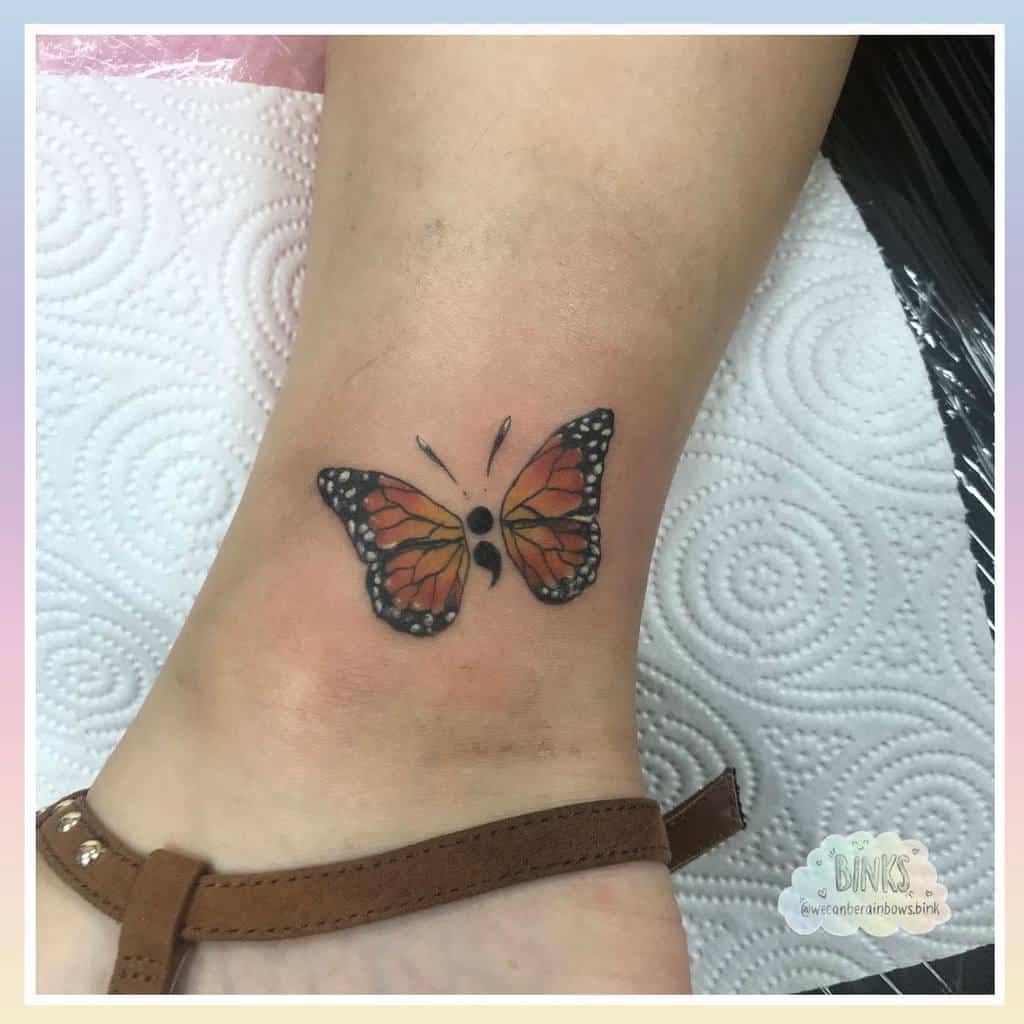 A beautiful orange and black semicolon butterfly tattoo on the ankle, symbolizing mental health awareness, resilience, and the continuation of life’s journey