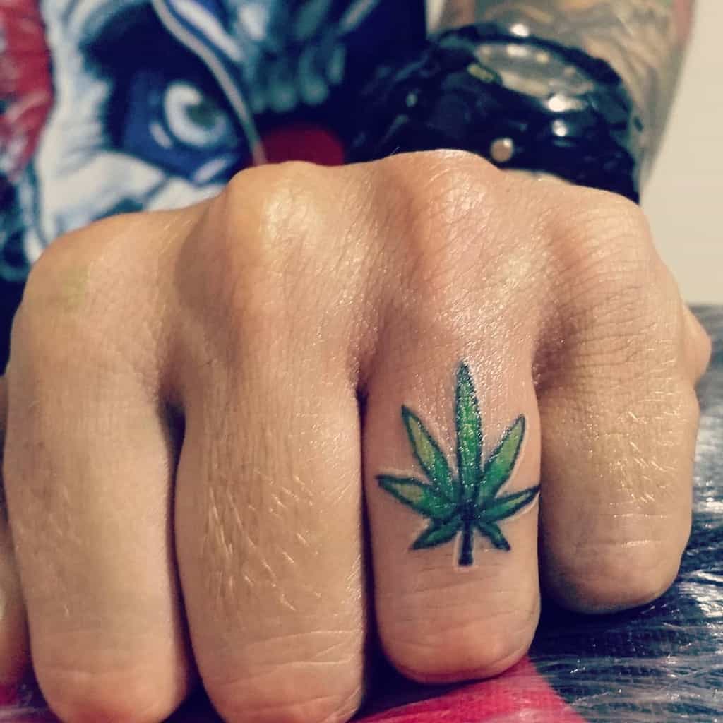 Hand with a small green cannabis leaf tattoo on the middle finger